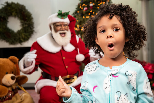 Portrait of a young African American standing in living room in shock as she sees Santa Claus behind her. Black Santa