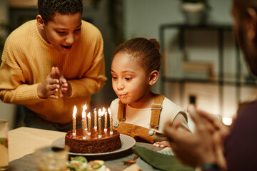 Portrait of cute little girl blowing candles on Birthday cake while celebrating with big happy...