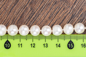 Close-up shot of a necklace made of pearl beads and a ruler on a wooden background.
