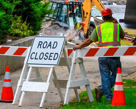 Hard hat construction worker talking on cell phone. standing next to road closed sign. 