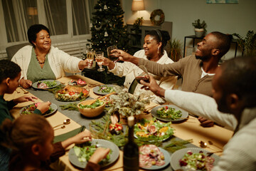 Fototapeta na wymiar High angle view at happy African-American family toasting with glasses while enjoying dinner together at Christmas