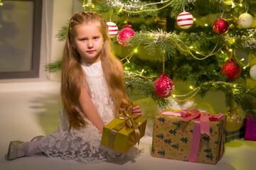 Little girl near the Christmas tree with a gift.