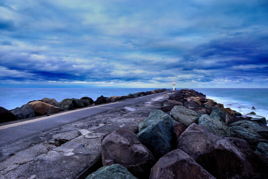Looking down length of rocky breakwater leading out to the ocean in evening