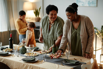 Waist up portrait of two African-American women serving table for family dinner party at home
