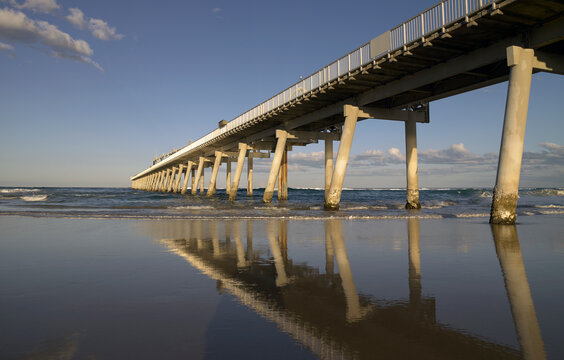 Reflections in the wet sand of long jetty streching out to sea