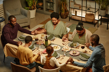 Plakat High angle view at big African-American family holding hands while saying grace during dinner party at home