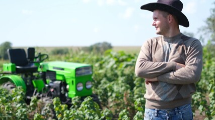 Young happy farmer rejoices at his new tractor. Man on the field near the green mini tractor.