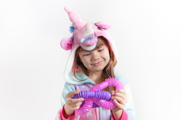 Cheerful little girl in unicorn pajamas plays in a popular toy poptube. An exciting children's game with multi-colored plastic pipes.