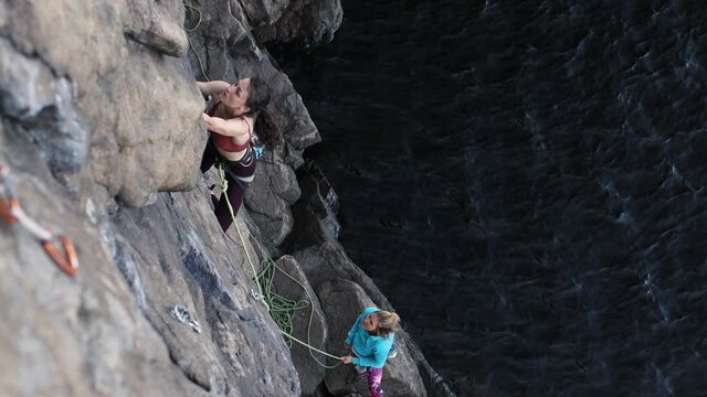 a girl climbs a rock above the water, a partner is belaying a friend, rock climbing on natural terrain