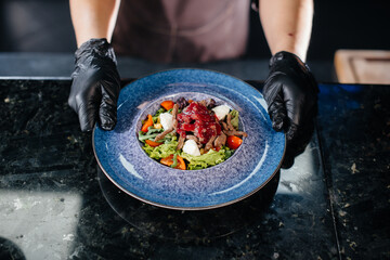 A professional chef serves a freshly prepared salad of tomato and veal greens with sauce in a gourmet restaurant close-up.