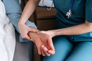Close-up cropped shot of unrecognizable female nurse checking pulse on wrist to sick senior male patient lying on bed in hospital room. Closeup top view of doctor checking mature patient pulse at home