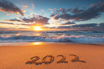 Fototapeta Happy New Year 2022 text, lettering on the beach sand at sunrise. obraz