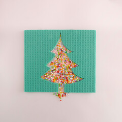 Christmas tree made of carved sponge cloth and multicolored party decoration. Creative christmas and new year celebration concept. Flat lay composition, sqare ratio.