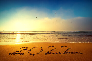 Happy New Year 2022 concept, lettering on the beach. Written text on the sea beach at sunrise.