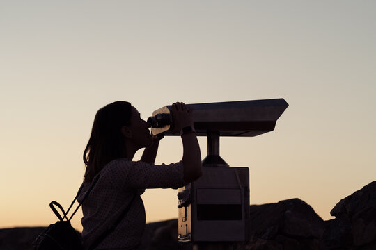 Young woman looking through a coin operated binoculars in the dark