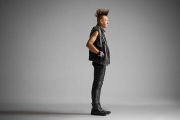 Full length profile shot of a punk man with a mohawk isolated on gray