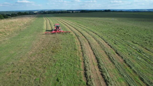 The farmer turns the grass with a hay rake attached to the tractor. Shot from a height.