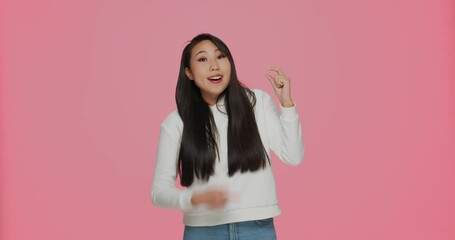 Happy asian girl showing with fingers small prices gesture, demonstrating little measurement on pink studio background