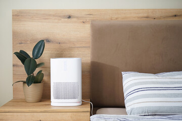 Modern air purifier in the bedroom by the bed, space for text.
