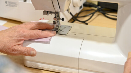 A woman sews a cloth with a sewing machine. The woman works in a factory. 