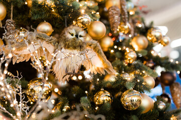 Obraz na płótnie Canvas The toy owl sits on a branch of a Christmas tree, which is decorated with golden balls and cones.
