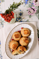 Meat pies with brie cheese on an oval platter. Linen tablecloth, viburnum in a vase.