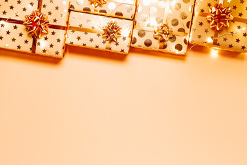 Gift boxes with golden bows and lights on peach background. Copy space for your text. Top view.