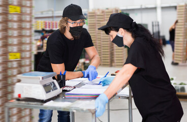 Diligent efficient positive manager in protective mask invites factory warehouse worker to sign documents.