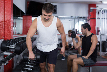 Fototapeta na wymiar Sporty man choosing dumbbells during weightlifting workout at gym