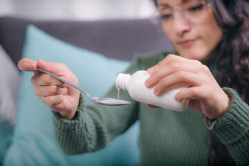 Close-up of a young woman's hands holding a cough syrup which she pours onto a spoon.