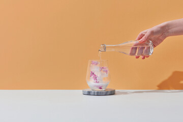 Woman pouring water in glass with pink flowers