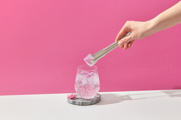 Woman putting ice cube with pink flower in glass