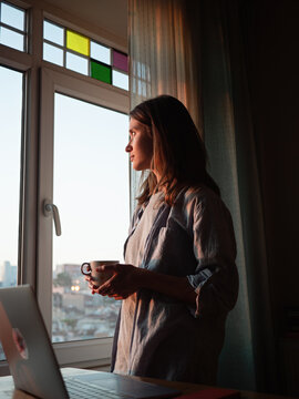 Woman with a coffee looking to the window at evening