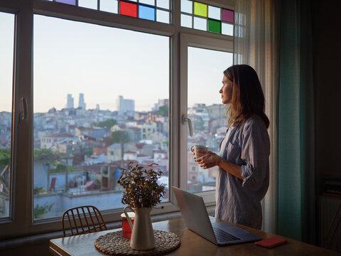 Woman with a coffee looking to the window at evening