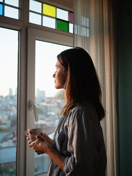 Woman with a coffee looking to the window at evening