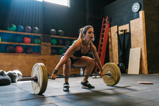 Muscular sportswoman deadlifting barbell during training