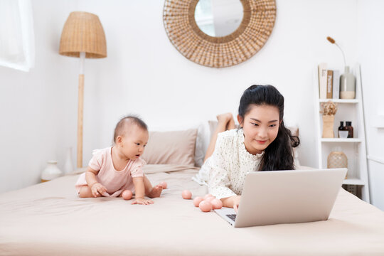 A young mother with a small child resting on the bed, with a portable laptop