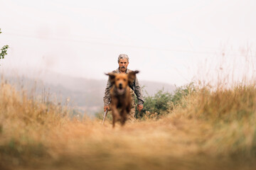 Mature hunting man and his dog chasing a prey across the field.