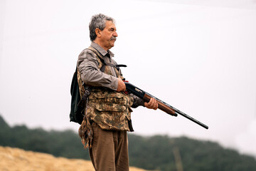 Mature hunting man holding a gun while searching for new preys.
