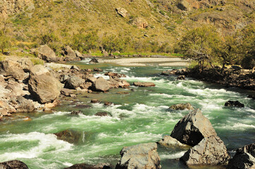 A winding bed of a turbulent mountain river of turquoise color, bending around stones, flows along...