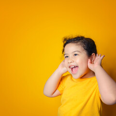 Little Asian girl holds her hand near her ear and listenings. Exciting face on Asian child girl. Exciting face on happy asian girl wear yellow shirt and listening to curious good news.