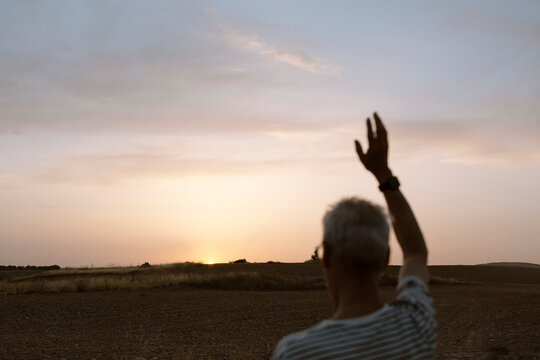 Back of man waving at the sun at sunset