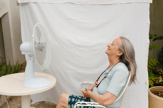 Grey-haired woman in front of fan outdoors