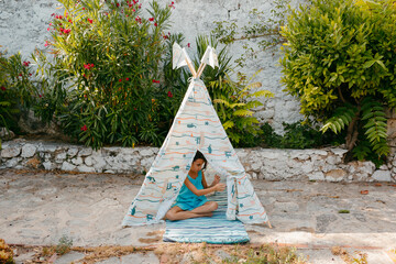 Kid inside toy tepee tent in a garden in sunlight
