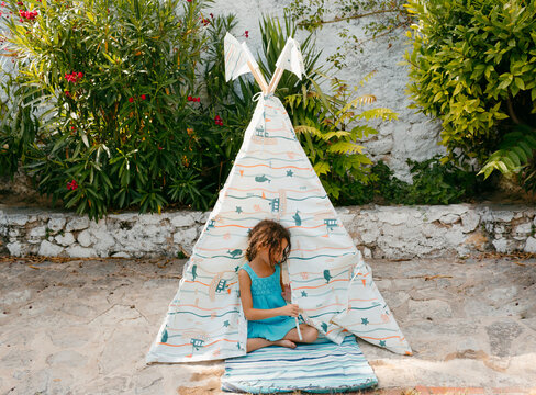 Kid in toy tepee tent in a garden in sinlight
