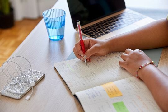 Woman with laptop taking notes in copybook