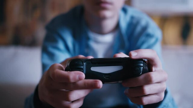 teen boy sitting on the sofa and playing playstation, joystick close-up, cinematic shot