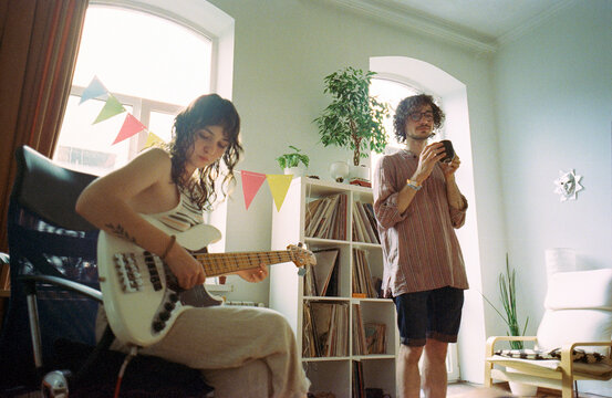 Woman playing bass guitar and man drinking coffee 