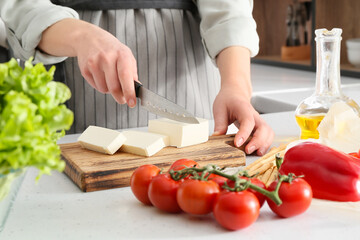 Obraz na płótnie Canvas Woman cutting feta cheese on table in kitchen