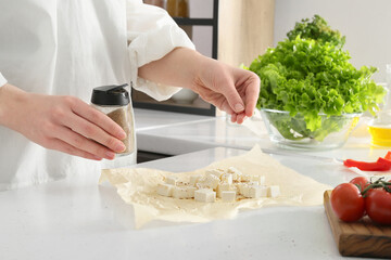 Woman putting spices into cut feta cheese on table in kitchen